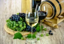 Mlado vino v Stopercih: napovedana analiza vzorca za tri evre in nasveti za nego Simbolična fotografija kozarcev belega in rdečega vina z grozdjem ob lesenem sodu